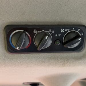 Car climate control panel: left temperature knob (blue-to-red), middle airflow direction knob, right fan speed knob with A/C button nearby and indicator light.