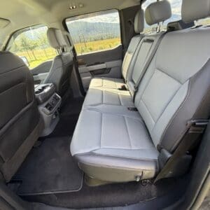 Rear passenger seating area in a pickup truck with light gray leather seats and countryside scenery visible through the windows.