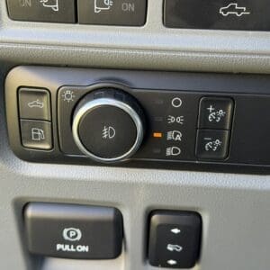 Car dashboard switch panel: left parking brake button labeled 'PULL ON', central round light control, and right lever with up/down arrows for auxiliary functions.