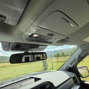 Interior of a pickup truck showing the overhead console, rearview mirror, and dashboard with a view of a grassy field and distant hills through the windshield.