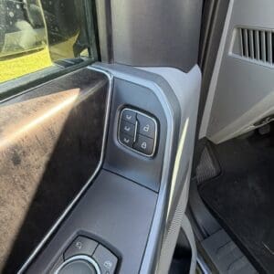 Close-up of the driver's door control panel: window, lock, and mirror adjustment controls near the armrest inside the car
