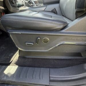 Driver seat with adjustment controls on the side (round lumbar knob, lever, and smaller switch) and black leather upholstery in a pickup truck interior.
