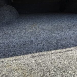 Car trunk lined with gray carpet; dark interior with BEDRUG logo on the right side.