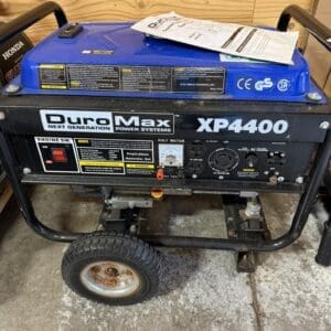 Blue DynoMax XP4000 portable generator on a wheeled metal frame in a workshop, with papers resting on its blue housing.
