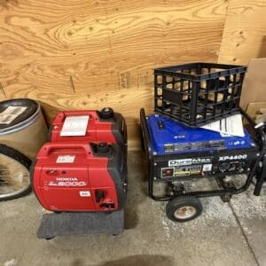 Red Honda EU2000i portable generator on a small dolly, beside a blue DuroMax XP4400 generator with a plastic crate on top in a cluttered garage workshop