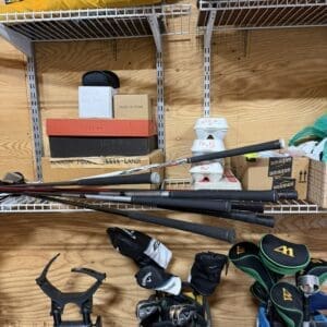 Garage shelving with stacked boxes and several golf bags and clubs on the floor below it.