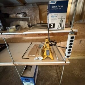 Workbench with a yellow hydraulic jack, wood pieces, and a box labeled 'Stack Jacks' on a shelf above it.