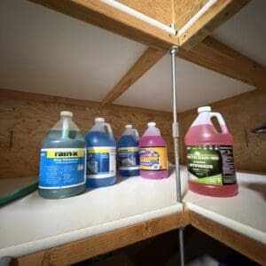Assorted car cleaning and antifreeze bottles lined up on a wooden garage shelf, under a sloped ceiling.