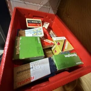 Red plastic bin filled with assorted small boxes of auto parts on a wooden floor/box lid nearby.