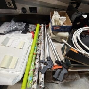 Cluttered workbench with clamps, wrapping paper rolls, a Skippy peanut butter box, cords, and a shoe on the floor.
