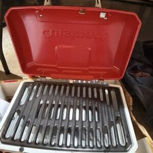 Open red portable grill with ribbed grilling grate and white body, ready for cooking indoors/indoors setting.