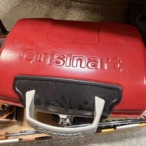 Red Cuisinart portable grill with a light gray carrying handle, stored on a wheeled cart in a garage or workshop space.