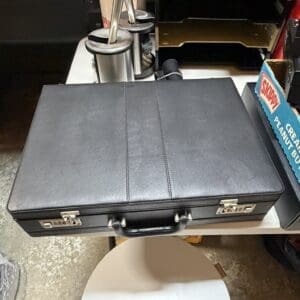Closed black briefcase with metal latches and a handle on a white round table in a store display.