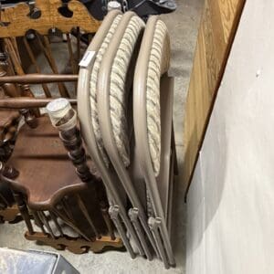 Beige folding chairs with striped cushioned seats stacked in a storage area beside a wall.