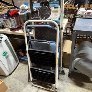 Rolling cart stacked with several black folding chairs in a cluttered workshop space.