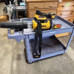 Yellow DeWalt cordless blower resting on a blue metal work cart in a cluttered workshop.