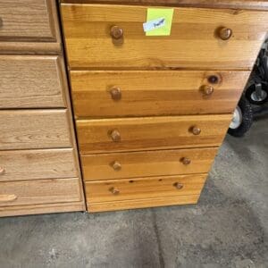 Six-drawer wooden dresser with round knobs, a cloth on top and a sticky note, in a garage/workspace.