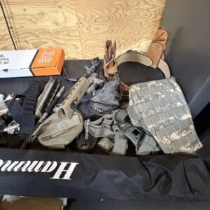 Assorted tactical gear spread on a table: holster, pouches, straps, and a camouflage plate carrier/vest subset.