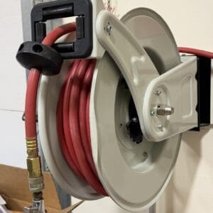 Red air hose coiled on a wall-mounted reel with a brass quick-connect fitting in a workshop setting.