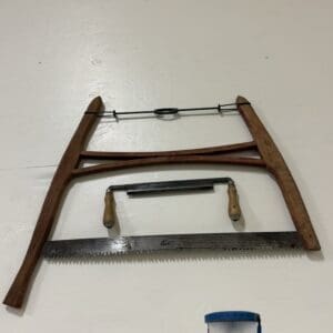Antique bow saw with wooden side frames and a long blade on a white surface, plus a smaller coping saw nearby.