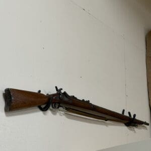 Antique wooden rifle mounted horizontally on a white wall as a display.