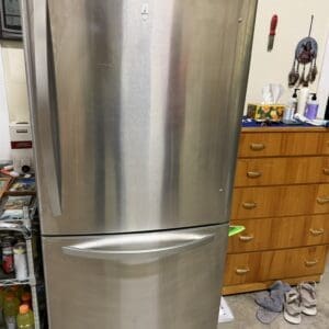 Stainless steel LG refrigerator with a bottom freezer in a cluttered home workshop area.