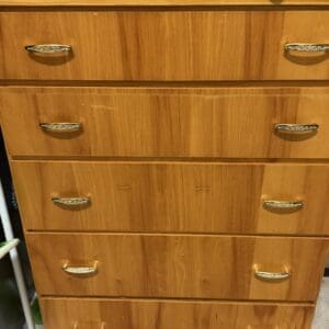 Wooden tall dresser with multiple drawers and ornate metal handles, cluttered with toiletries and items on top.