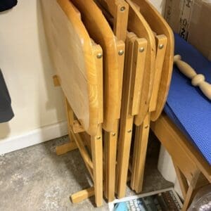 Stacked wooden folding chairs in a storage room corner, with a blue mat and a magazine on the floor.