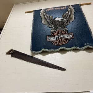 Blue Harley-Davidson banner with an eagle, hung from a wooden rod on a white worktable near a handsaw.