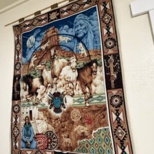Colorful tapestry showing galloping horses over a desert canyon, with a blue-toned, large portrait in the clouds and geometric border patterns.