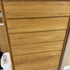 Oak wood dresser with seven shallow drawers standing in a room, items on top.