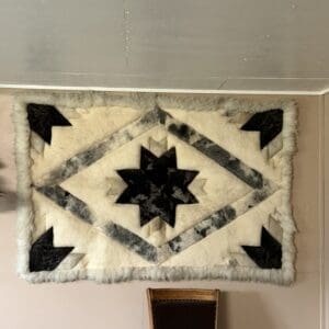 Wall-mounted shag rug with a black starburst center and gray diamond border on a pale wall, fringed edges visible at the sides.