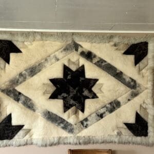 Fluffy cream rug with a black star centerpiece and gray diamond border, finished with a light gray fringe edge on a light floor.