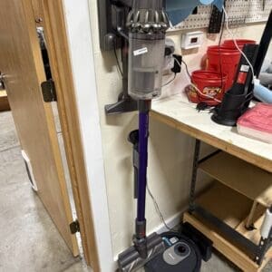 Dyson cordless stick vacuum mounted on a wall with charging dock in a workshop.