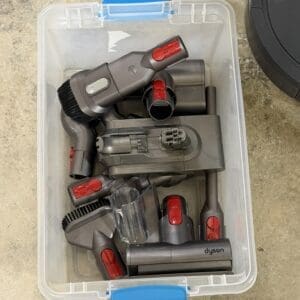 Plastic storage bin containing a collection of Dyson vacuum cleaner attachments and fittings in gray and red.