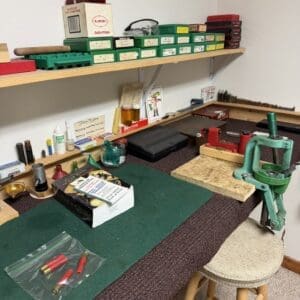 Workbench with a green reloading press, brass cartridges, and ammo boxes on the shelves above.