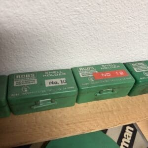 Row of green RCBS shell holders lined up on a wooden shelf against a textured wall, showing No. 10 and No. 12 labels.