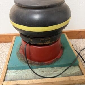 Vintage electric device with a black rounded top, yellow stripe, and red motor base on a wooden frame; power cord visible.