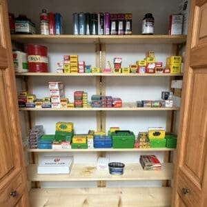 Open closet with wooden shelves filled with small boxes of hardware, cans, and organizers; green and yellow plastic tool boxes on the lower shelves.