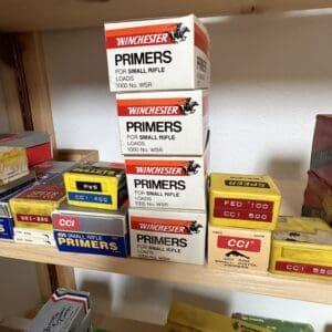 Stack of Winchester primers boxes for small rifle loads on a wooden shelf in a storage room warehouse setting.