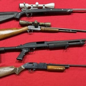 Four rifles on red fabric: top—bolt-action with scope; second—lever-action with wooden stock and scope; third—pump-action shotgun with pistol grip; bottom—classic lever-action with wood stock.