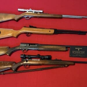Five rifles laid out on a red surface, ranging from bolt-action to lever-action with scopes and optics visible.