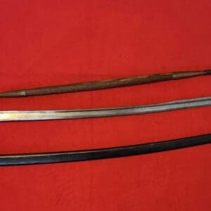 Three historical blades laid on a red surface: a long spear, a curved sword with a brass guard, and a black sheath.