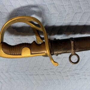 Vintage sword or bayonet with gold-colored guard and black grip on a quilted blue surface, side view.