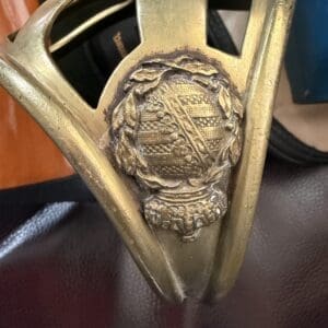 Brass military-style belt buckle with a circular, laurel-wrapped crest at center on a brown belt.