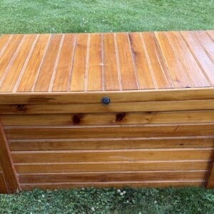 A wooden outdoor storage chest with a hinged lid sitting on green grass.