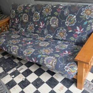 Sofa with wooden arms and a dark floral patterned fabric on a checkered floor.