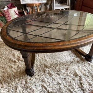 Round wooden coffee table with glass top and grid pattern, standing on a shaggy beige rug in a living room.