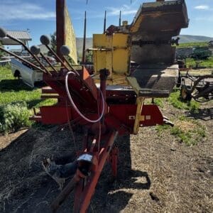 LOT 3 2 - Montana Auctions by Kevin Hill Red and yellow farm implement on dirt with a cat nearby, under a blue sky at a rural yard edge.