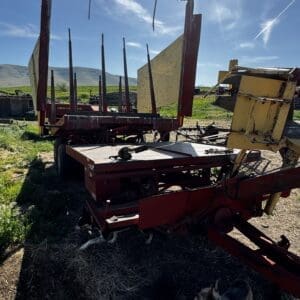 LOT 3 4 - Montana Auctions by Kevin Hill Abandoned red farm equipment with a yellow hopper in a sunlit field and distant hills; a small dog nearby.